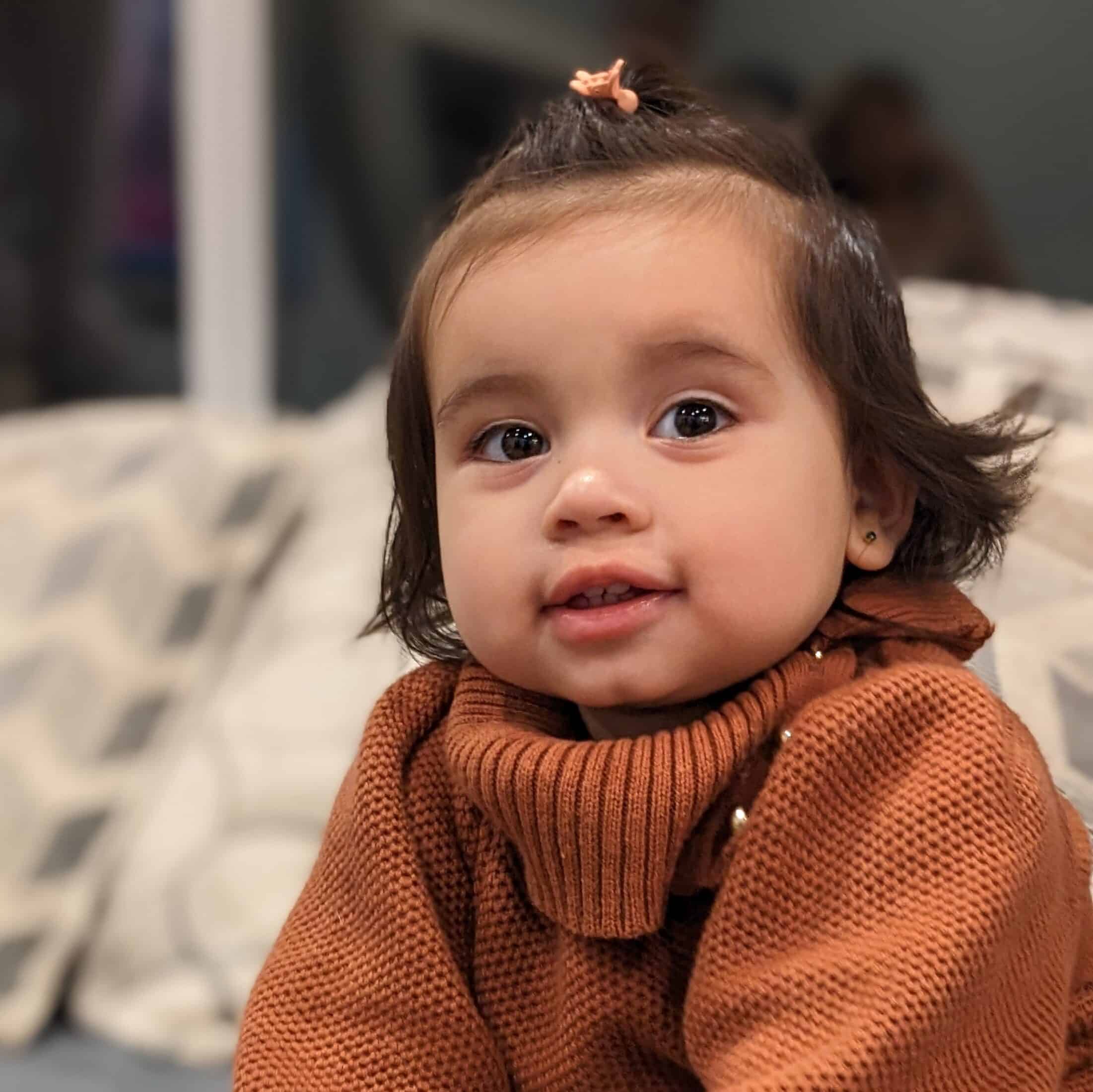 A little girl in a brown sweater sitting on a couch.